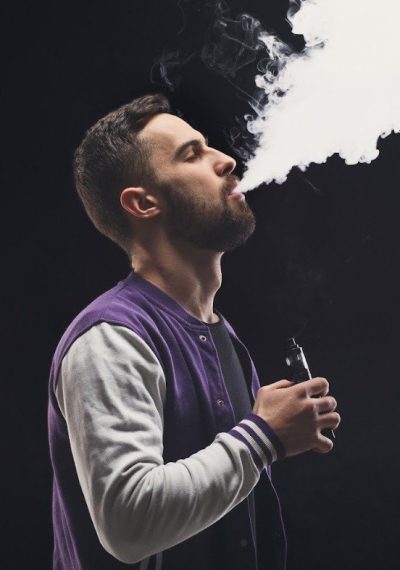 Hombre usando un vaporizador en Estanco Osuna, generando vapor en un entorno oscuro.